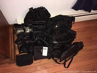 Various black handbags, backpacks, and totes arranged on floor showing different styles and sizes.