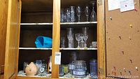 Wood cabinet with multiple shelves containing stemware, glass casserole dishes, canisters, and plastic containers