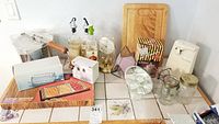 Full lot view showing popcorn popper, can opener, cutting board, mason jars, glass creamer, soap dispensers, salt and pepper shakers, boxed snacks, and Flair serving set in background