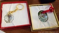 Photo showing Swarovski round faceted crystal Christmas ornament with holographic design, attached to red ribbon, in gold box