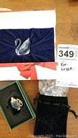 Swarovski crystal swan in display box with accompanying crystal hearts in black pouch nearby.