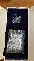 Small Swarovski swan crystal figurine displayed nestled in navy velvet inside a white box with a sealed plastic bag of loose crystals alongside.