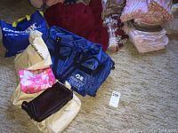 Photo of cloth tote bags including beige floral tote, two blue nylon duffel bags including one Princess Cruises branded, folded linens, quilts and afghans in red and beige shades.