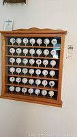 Front view of oak curio cabinet mounted on wall showing six shelves with 48 golf balls on tees inside.