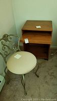View of the wood night stand with pull-out tray and metal frame chair with beige cloth seat next to it on carpeted floor.