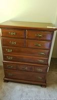 Front view of wooden dresser with seven drawers and ornate brass handles.