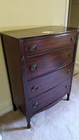 Full view of the vintage wooden dresser showing four drawers and metal ring handles against a wall.