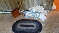 Photo showing braided rug, walking canes, framed embroidery art, wooden magazine box, and pile of curtains