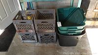 Photo showing six black plastic milk crates stacked in two layers, and three plastic storage totes stacked with lids beside them.