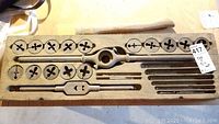 Full view of vintage tap and die set showing round dies, taps, and T-handle die stocks inside wooden case.