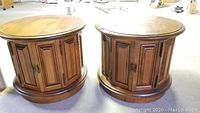 Two matching round wooden end tables with paneled cabinet doors shown together.