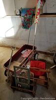Red Radio Flyer wagon with black wheels, garden flags, magazine rack with woven basket, and inspirational plaque grouped together.