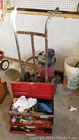 Metal hand truck, red toolbox with tools in front, wet/dry shop vacuum in background