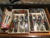 Drawer with organized flatware including forks, spoons, steak knives with stag horn handles, and kitchen utensils showing condition and variety