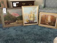 All three framed oil paintings arranged on carpeted floor in front of furniture.