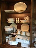 Overview of white Lenox china with platinum rim displayed on wood shelves, includes platters, bowls, plates, cups, saucers, sugar bowl, creamer, salt and pepper sets.