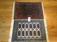 Two modern oriental rugs laid on wooden floor, one darker floral with red border and one lighter with geometric medallion pattern.