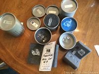 Overview of the lot of 6 Swarovski crystal miniature figurines in original metal tins with foam inserts, including rabbit, squirrel, two trees, and three buildings.