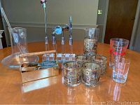 Photo of entire barware set on wooden table showing decanter, cocktail tools, glasses, pitcher, and brass box with corkscrew