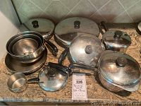 Full view of Revere Ware copper-clad stainless steel pots and pans with black handles and glass lids, including small to large sizes and a small measuring cup.