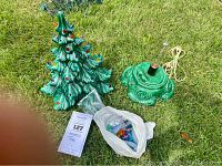 Photo of vintage green ceramic Christmas tree with colorful bulbs and ceramic base with cord, plus extra bulbs in plastic bag on grass.