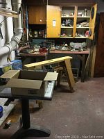 Overview of workshop showing wooden work table, pegboard with tools, countertop cabinets in background, black cafe-style table