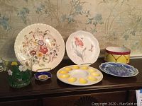 Front view of five plates on display, including floral designs and ceramic drum-shaped bowl, plus glass ice bucket and small blue trinket dish.