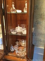 Two cut crystal decanters on top shelf of wooden cabinet