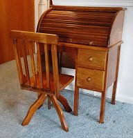 Child's oak rolltop desk with chair positioned in front and side angled view showcasing rolltop and drawers.