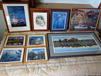 Nine framed art pieces laid on mattress including various Western and nature scenes.