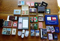 Photo showing entire collection of 42 decks of playing cards arranged on a wooden table, including boxed sets, vintage bicycle boxes, commemorative and themed decks, and a floppy disk.