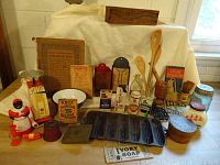 Wide view showing most of the vintage kitchen items including flour sieves, spice tins, iron muffin pan, wooden utensils, and labeled boxes.