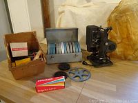 Kodak Kodascope Eight movie projector, metal case of reels, movie film, projector lamp box, and film reels on floor