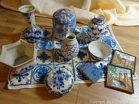 All 14 pieces arranged on patterned cloth showing full assortment including vases, covered jars, bowl, hexagonal dish, and scenic tiles