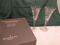 Two crystal toasting flutes with detailed cut designs standing on a table next to the original dark grey Waterford Crystal Millennium Collection gift box.