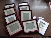 Eight reddish-brown wood 8x10 frames with installed 5x7 mats laid out on floor surface, showing condition and quantity.