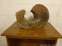 Front view of sculpture on wooden cart showing curved abstract form and wood grain on cart surface.