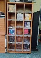 Front view of light oak CD storage cabinet showing 18 sliding trays with various CDs inside some slots.