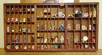 Wide view of two wooden printer type trays filled with diverse small miniature decorative items of various types, sizes, and colors.