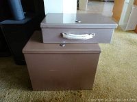 Photo of two stacked fire-resistant metal file boxes showing exterior with closed lids and handle on smaller box