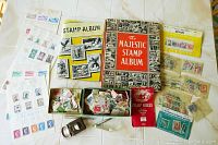 Two stamp albums, numerous loose stamps in envelopes and sleeves, plus stamp collecting accessories spread on a white surface.
