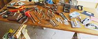 Wide view of various pliers, wood planes, wrenches, staple guns and other assorted tools spread on table.