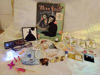 Includes assortment of vintage jewelry, collectibles, cosmetics, cocktail souvenirs, handkerchiefs, reading glasses, notepads, and the book 'Miss Sniff'