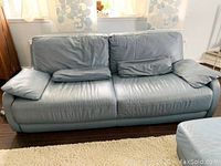 Wide front view of two-seat leather sofa with loose cushions and padded arms