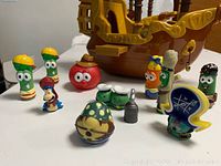 Close-up of 10 colorful Veggie Tales character figures and pirate hook, standing in front of pirate ship