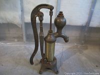 Front view of cast iron hand pump with brass cylinder, mounted on three-footed base