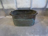 Copper boiler with visible green aged patina, dents, discoloration, and handles on sides, photographed from one angle.
