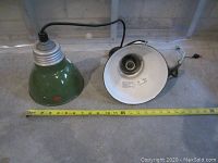 Photo of two green metal drop cord light fixtures side by side with measuring tape showing approx. 8 inches diameter.