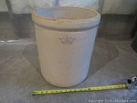 Full view of beige 6 gallon stoneware crock with measuring tape indicating size approximately 12 inches diameter and 15 inches tall.