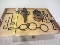 Photo of vintage wooden pulleys and various iron hooks and rods displayed on a tray with measuring tape for scale